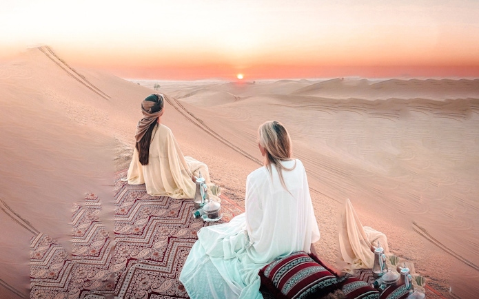 Two people sitting on a carpet in Abu Dhabi desert at sunrise during a morning safari.