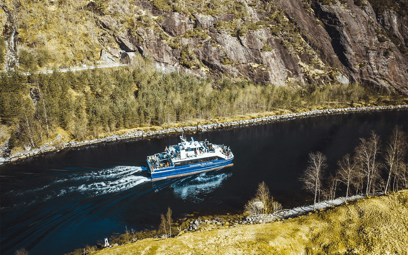 Mostraumen Fjord Cruise boat sailing through narrow fjord with rocky cliffs and trees in Norway.