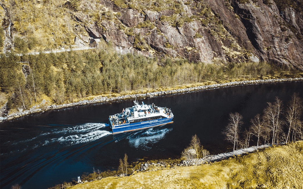 Mostraumen Fjord Cruise boat sailing through narrow fjord with rocky cliffs and trees in Norway.