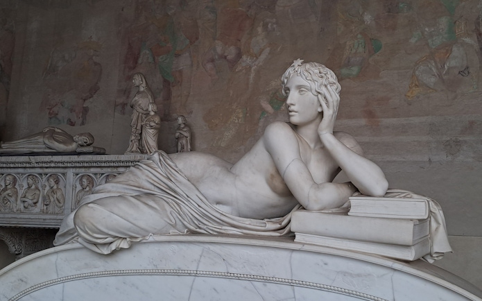 Marble statue in Pisa's Field of Miracles, depicting a reclining figure with books.