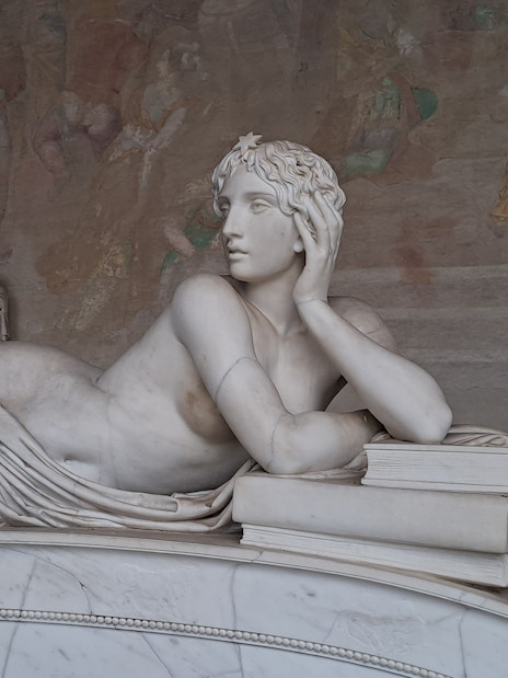 Marble statue in Pisa's Field of Miracles, depicting a reclining figure with books.