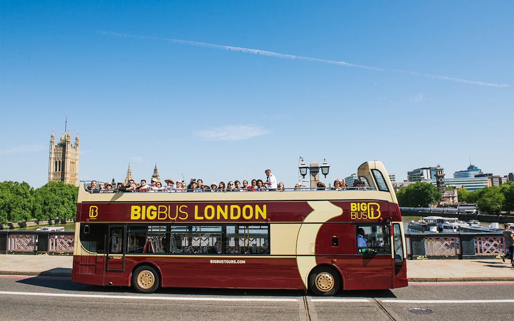 Big Bus tour in London with passengers, passing by the Houses of Parliament.