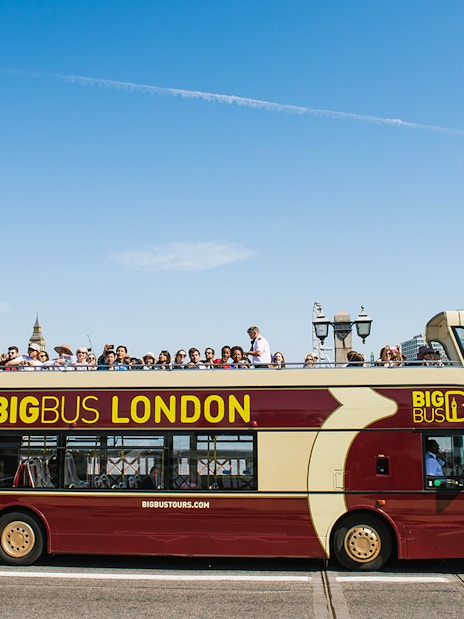 Big Bus tour in London with passengers, passing by the Houses of Parliament.