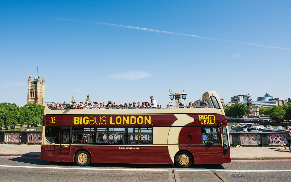 Big Bus tour in London with passengers, passing by the Houses of Parliament.