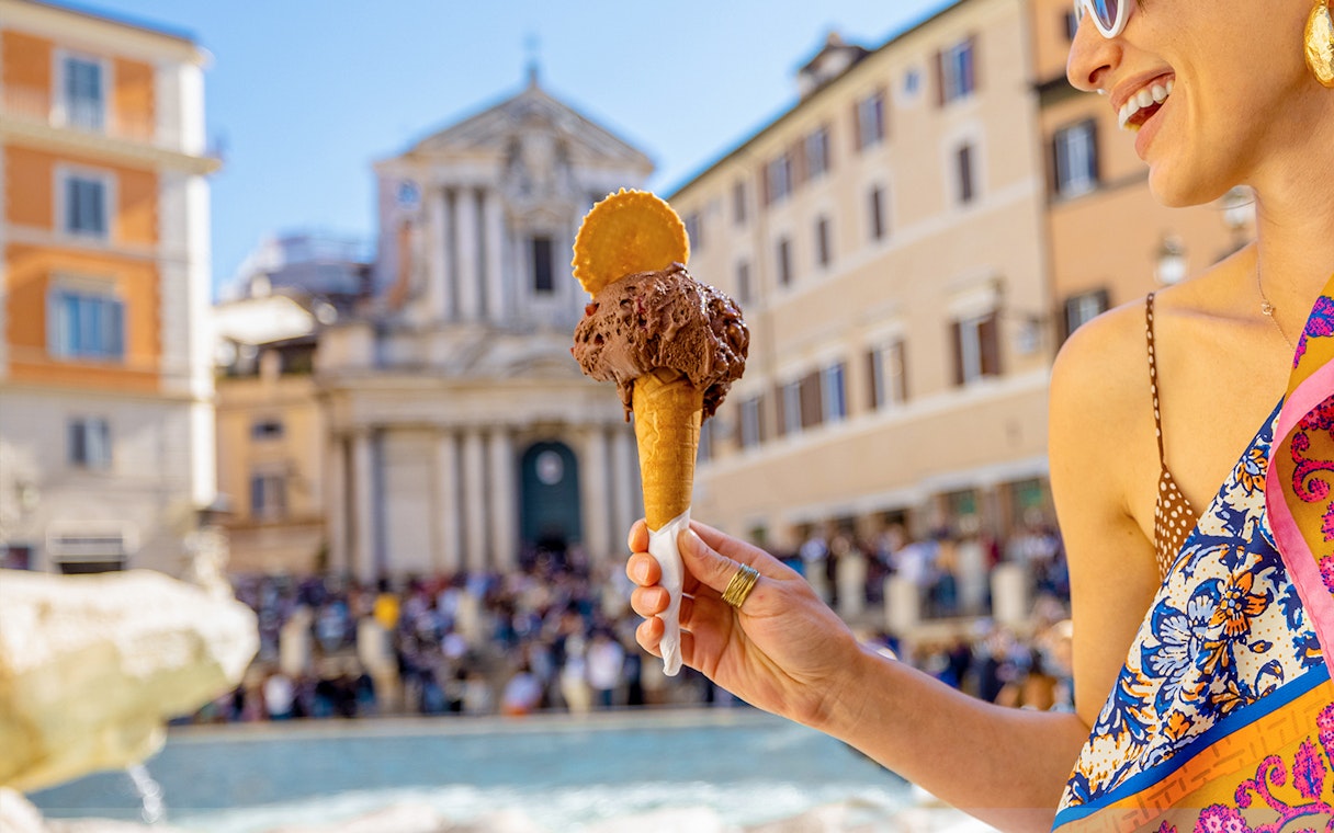 Gelato cone held in front of a historic building in Rome during summer.