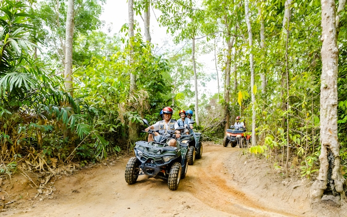 People riding quad bikes through a lush forest trail at Flying Hanuman.