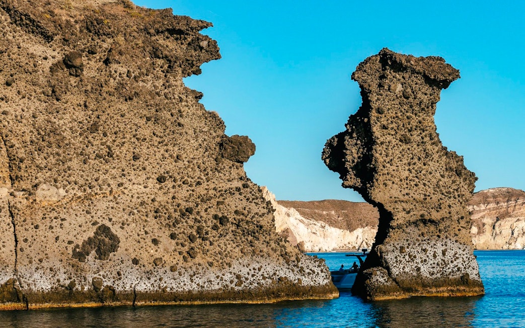 Indian Rocks formations along Santorini's southern coast with a boat in the sea.