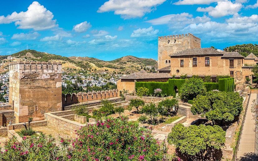 Alhambra fortress gardens and towers in Granada, Spain, with scenic hillside view.