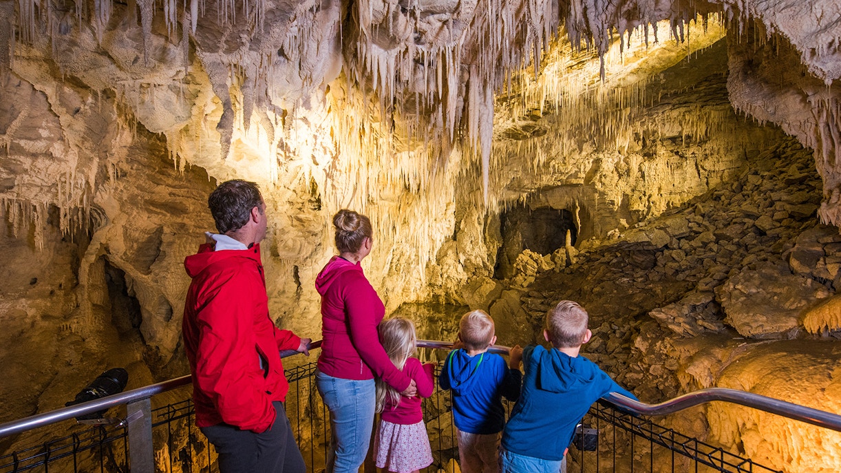 Visitors exploring the illuminated stalactites and stalagmites inside Aranui Cave, New Zealand.