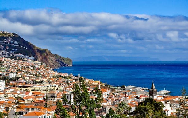 Funchal coastline view with red-roofed buildings and ocean, Madeira, Portugal.