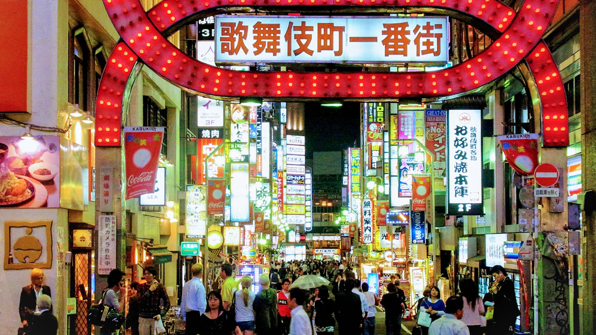 Crowded street in Shinjuku Kabukicho entertainment district with neon signs and people walking.