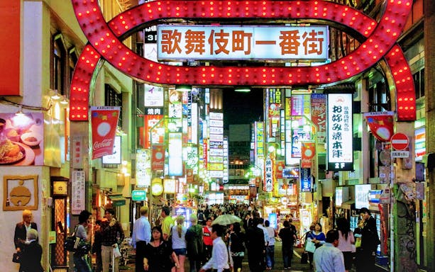 Crowded street in Shinjuku Kabukicho entertainment district with neon signs and people walking.
