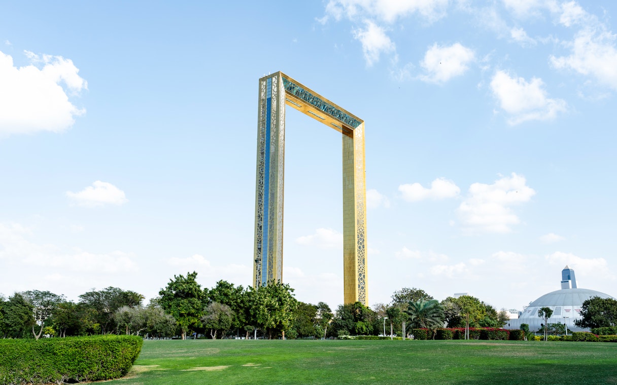 Dubai Frame towering in Zabeel Park under a sunny blue sky with clouds.