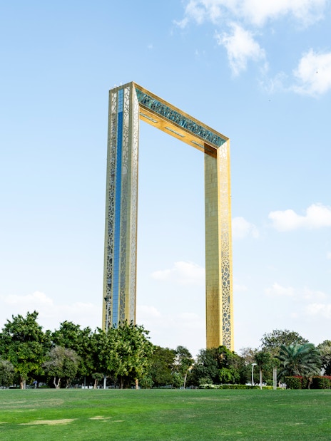 Dubai Frame towering in Zabeel Park under a sunny blue sky with clouds.