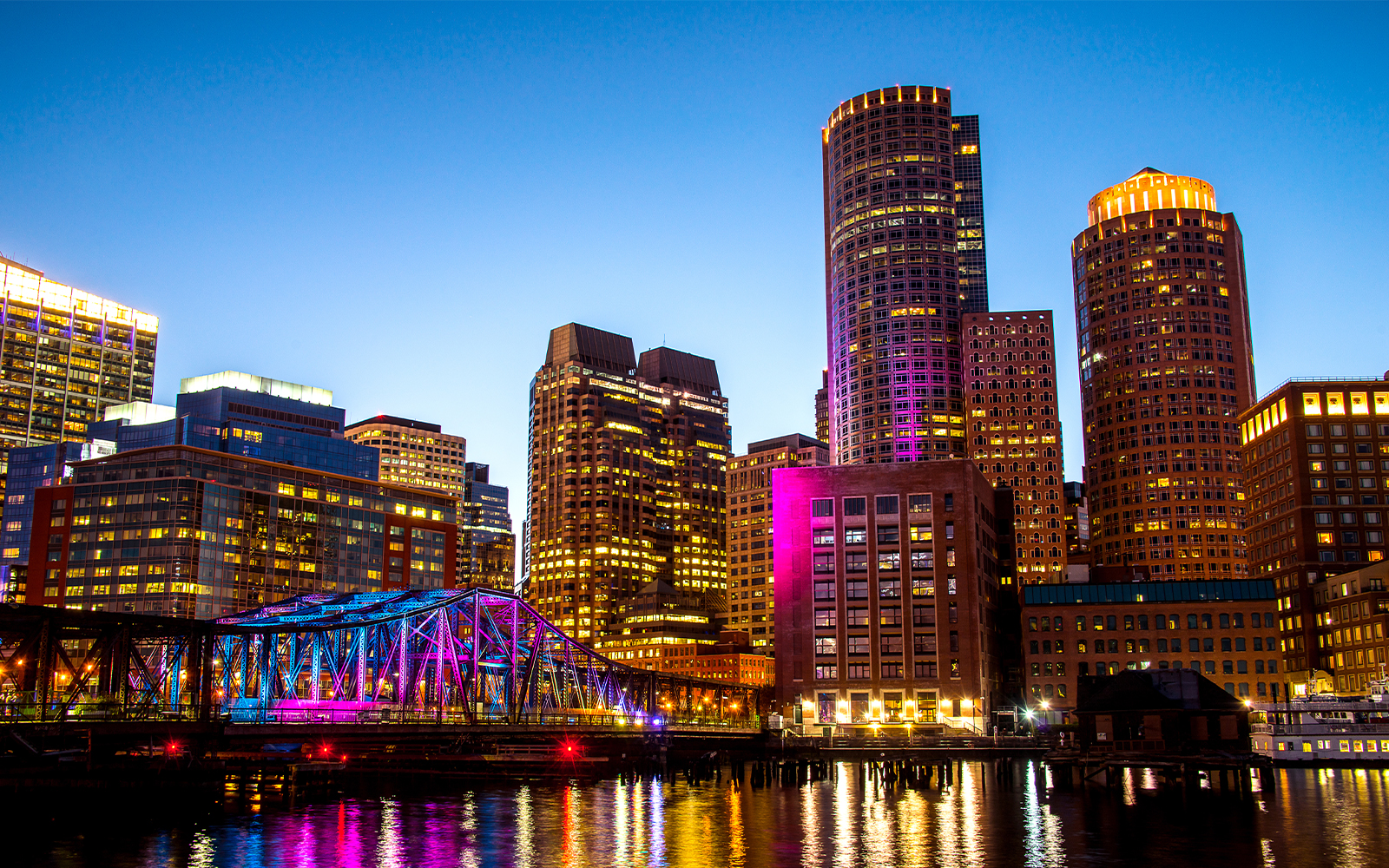 Boston Seaport skyline with illuminated bridge and buildings at night.