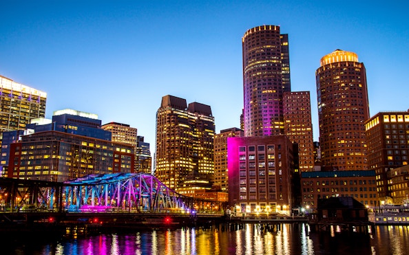 Boston Seaport skyline with illuminated bridge and buildings at night.
