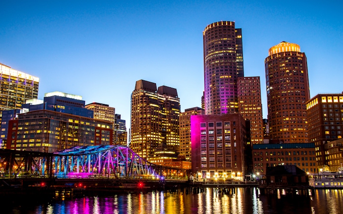 Boston Seaport skyline with illuminated bridge and buildings at night.