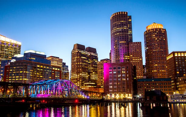 Boston Seaport skyline with illuminated bridge and buildings at night.
