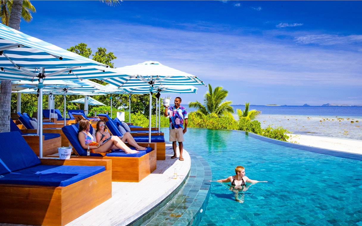 People relaxing on lounge chairs by the pool at Malamala Beach Club, Fiji.