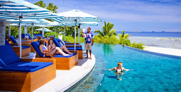 People relaxing on lounge chairs by the pool at Malamala Beach Club, Fiji.