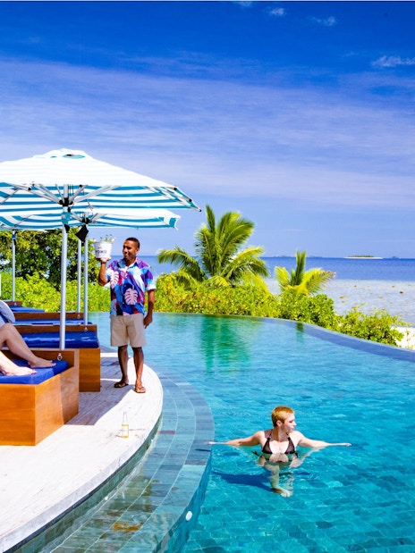 People relaxing on lounge chairs by the pool at Malamala Beach Club, Fiji.