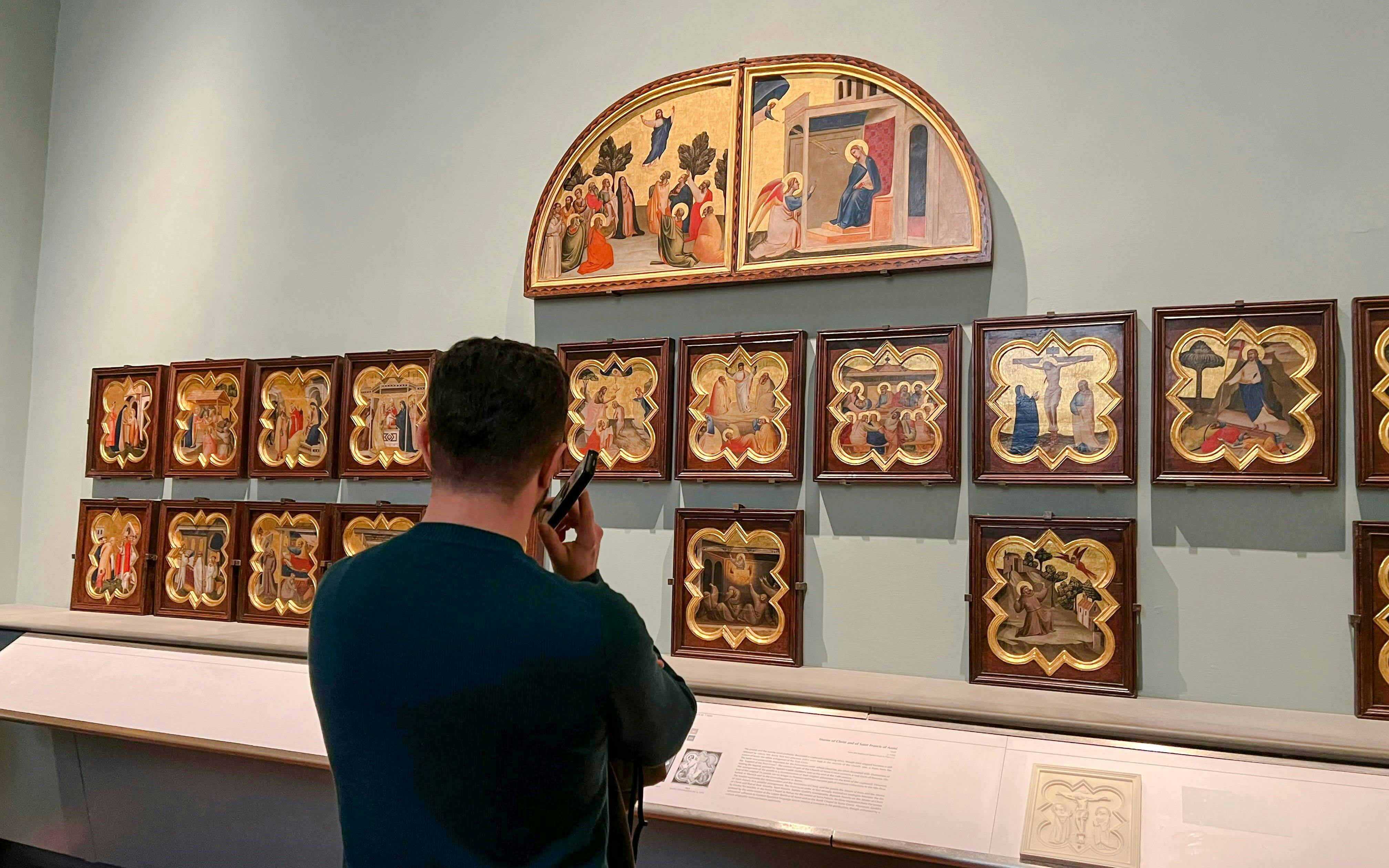 Visitor using audio guide at Academia Gallery, viewing religious paintings, Florence.