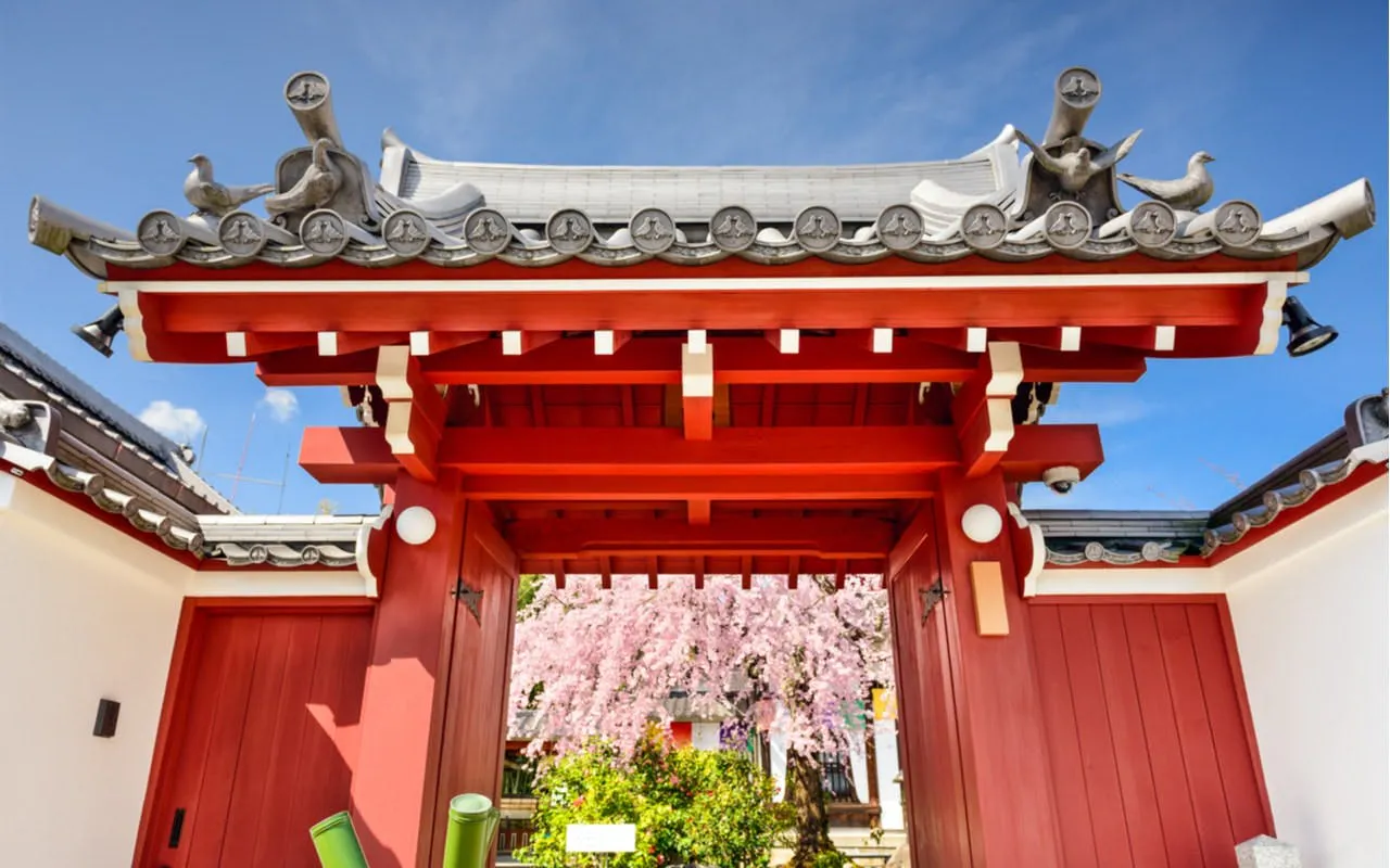 Red torii gate with cherry blossoms in Osaka, Japan, part of a self-guided city exploration game.