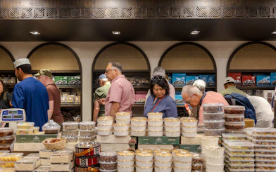 Tourists exploring a traditional market in Muscat, Oman, with local sweets and products on display.
