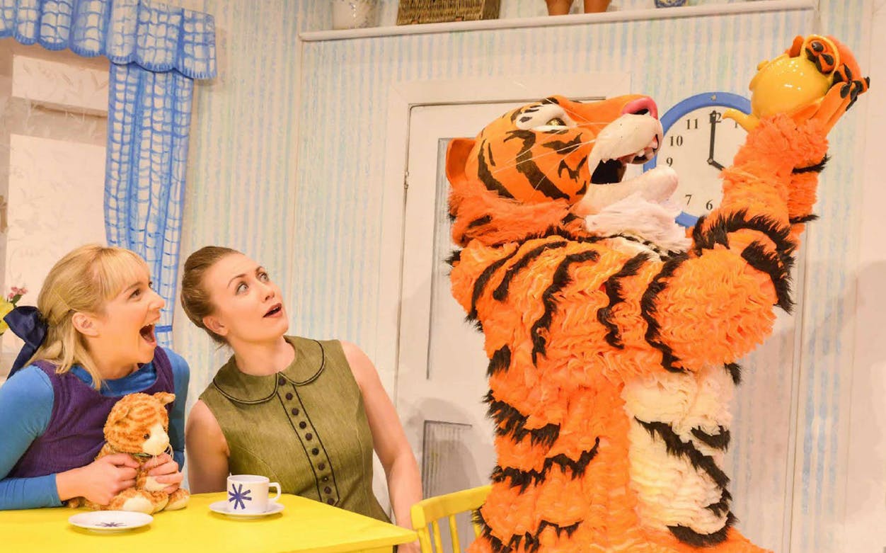 Tiger character holding teapot with two surprised women at a table, from "The Tiger Who Came to Tea" show.
