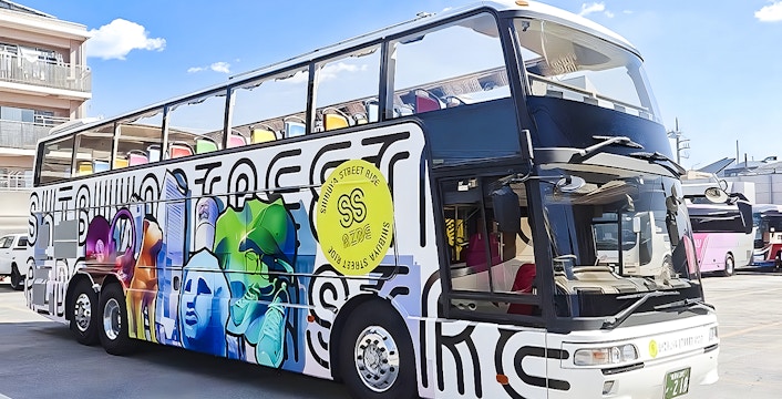 Double-decker bus with colorful graffiti design in Tokyo parking area.