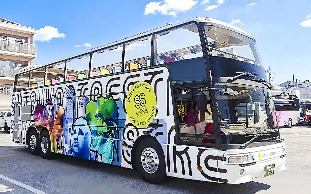 Double-decker bus with colorful graffiti design in Tokyo parking area.
