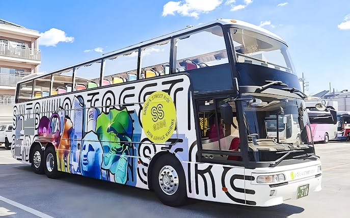 Double-decker bus with colorful graffiti design in Tokyo parking area.