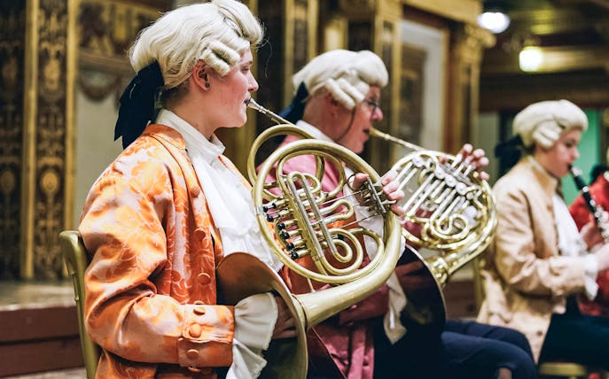 Musicians in period costumes playing French horns at a Mozart orchestra concert.
