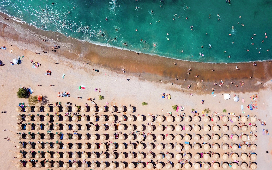Aerial view of Agios Nikolaos beach with sun umbrellas and swimmers, Anavysos, Athens Riviera, Greece.