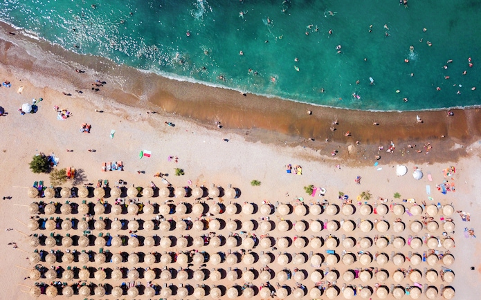 Aerial view of Agios Nikolaos beach with sun umbrellas and swimmers, Anavysos, Athens Riviera, Greece.