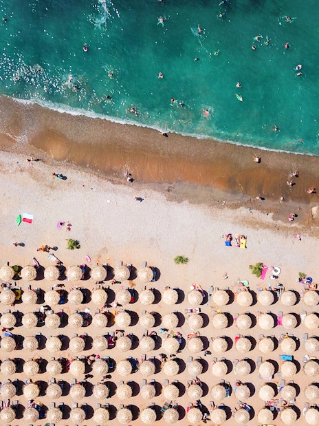 Aerial view of Agios Nikolaos beach with sun umbrellas and swimmers, Anavysos, Athens Riviera, Greece.