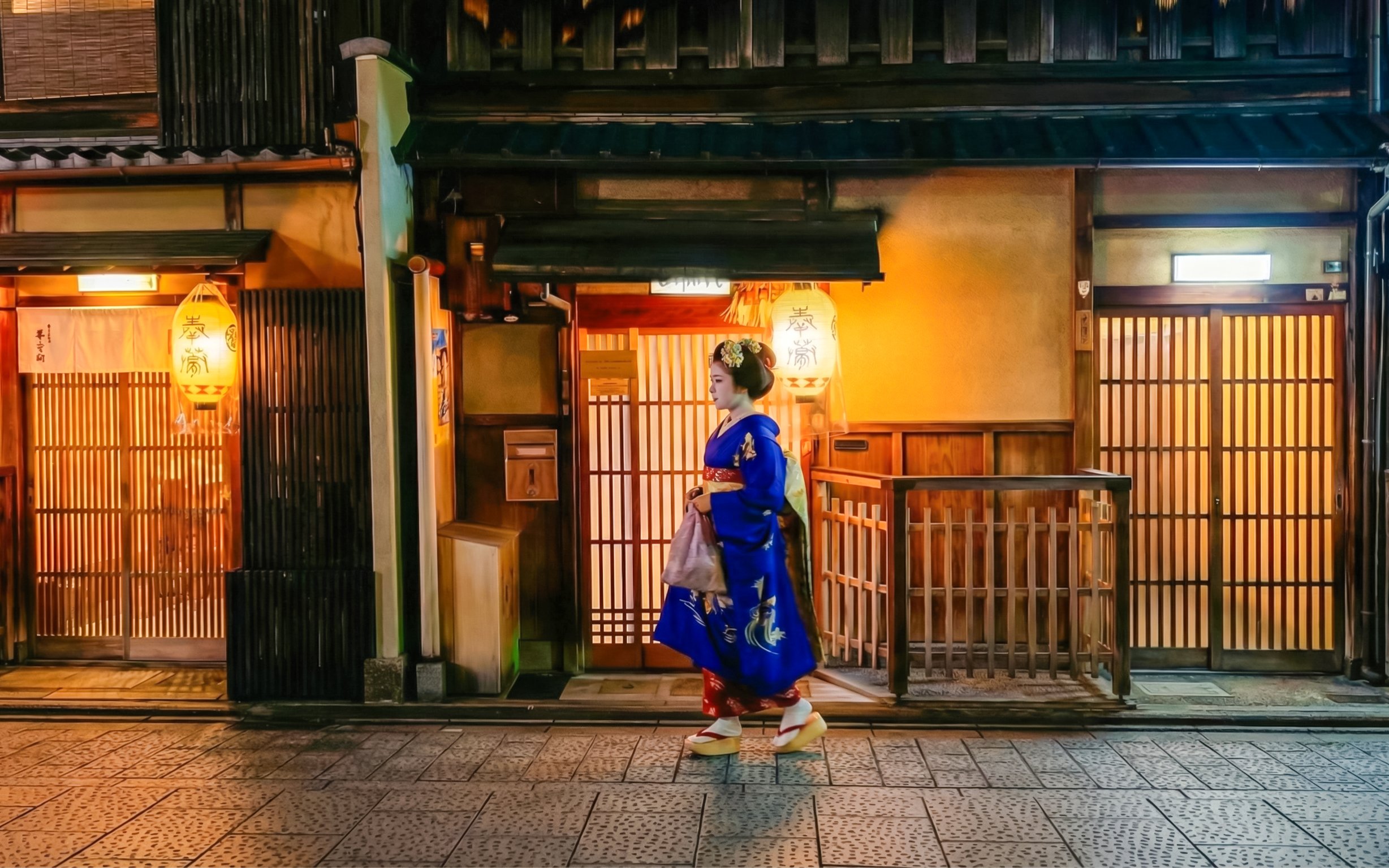 Geisha walking past traditional wooden buildings in Gion district, Kyoto.