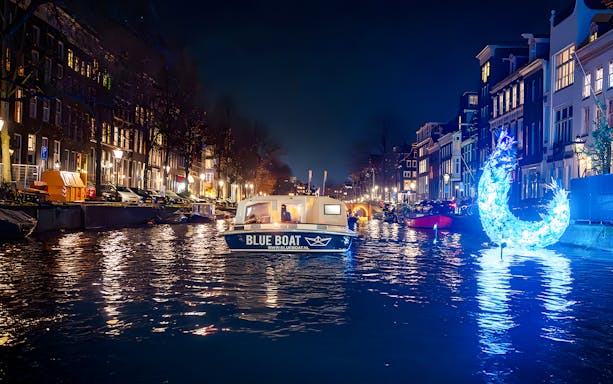 Amsterdam canal with illuminated art installation during Light Festival evening cruise.