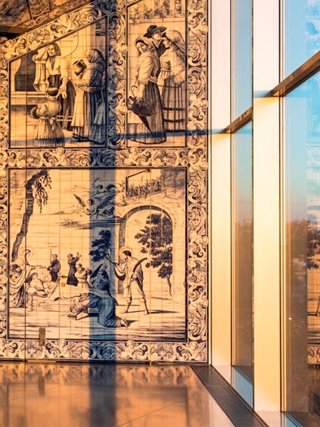 Azulejo tiles in a Porto building with sunset reflections on glass windows.