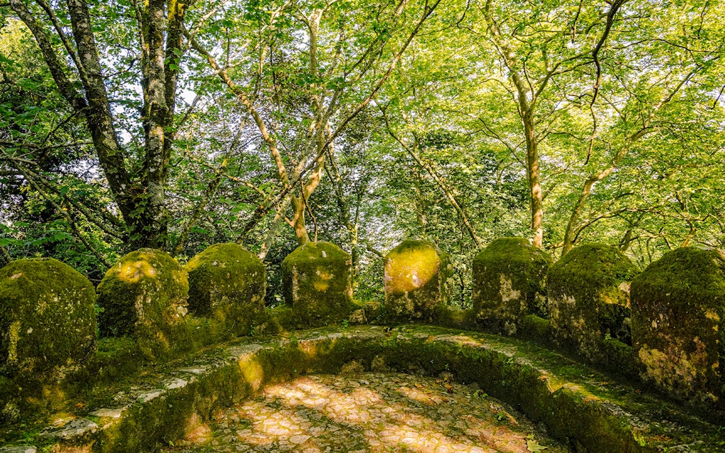 Moss-covered stone walls of Moorish Castle's second ring in Sintra, Portugal, surrounded by trees.