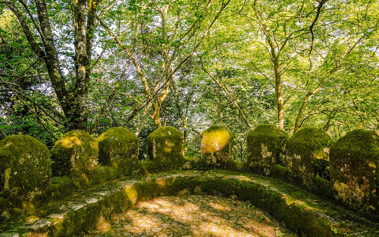Moss-covered stone walls of Moorish Castle's second ring in Sintra, Portugal, surrounded by trees.