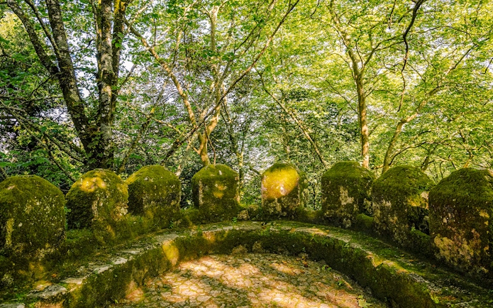 Moss-covered stone walls of Moorish Castle's second ring in Sintra, Portugal, surrounded by trees.