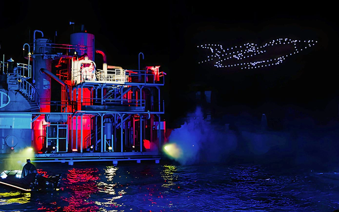 Parque Warner night drone show with illuminated building and water reflections.
