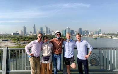 Group of tourists on a bridge with Ho Chi Minh City skyline during Saigon Hidden Gems Day Tour by Scooter.