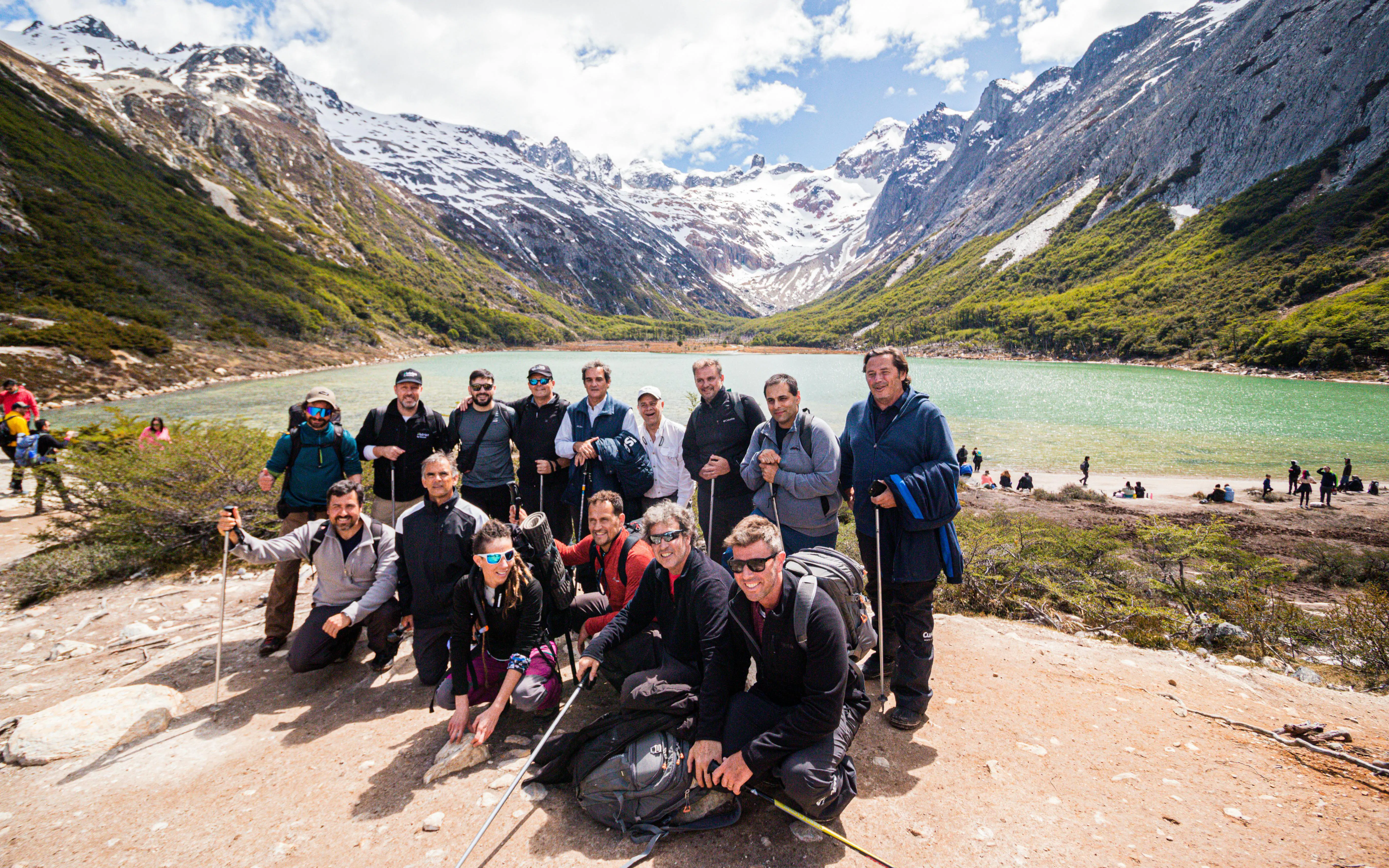 Group of hikers at Esmeralda Lake with snow-capped mountains in the background.