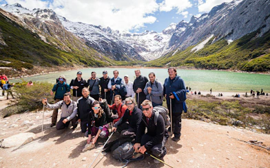 Group of hikers at Esmeralda Lake with snow-capped mountains in the background.