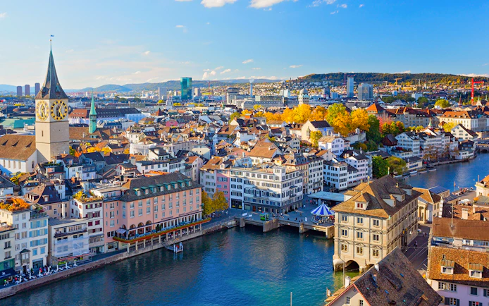 Zurich cityscape with Limmat River and historic buildings under a clear blue sky.