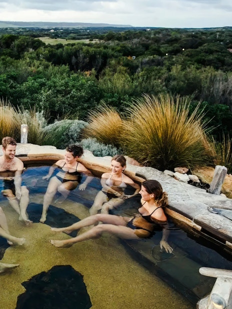 Group relaxing in a hot spring pool at Peninsula Hot Springs, surrounded by lush greenery.