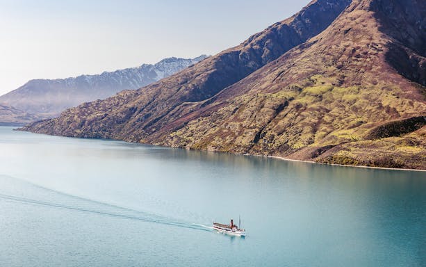 Boat cruising on Lake Wakatipu with snow-capped mountains in the background, Queenstown, New Zealand.
