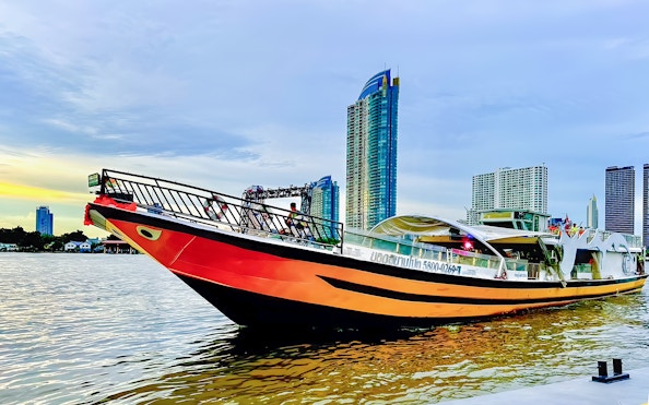Yodsiam sightseeing boat on a river with city skyscrapers in the background.